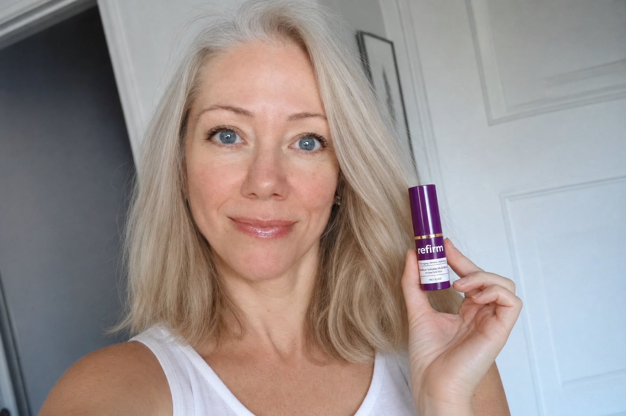 Woman applying Refirm Calcium Balm to her undereye area, smiling